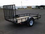 Pillowle 6’4” x 10’ utility trailer with black metal frame and wooden bed, suitable for carrying goods and equipment.